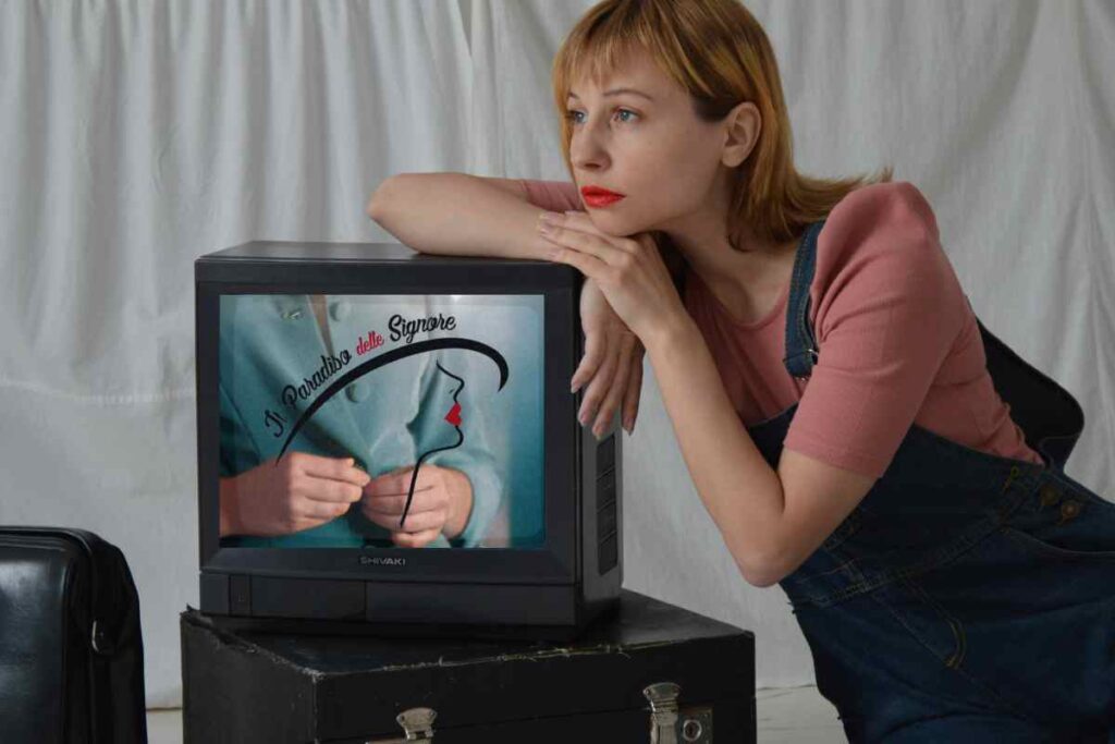 donna appoggiata su una vecchia tv che trasmette Il Paradiso delle Signore