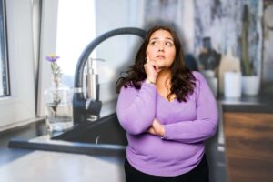 bicchiere di acqua accanto a lavandino e donna che pensa