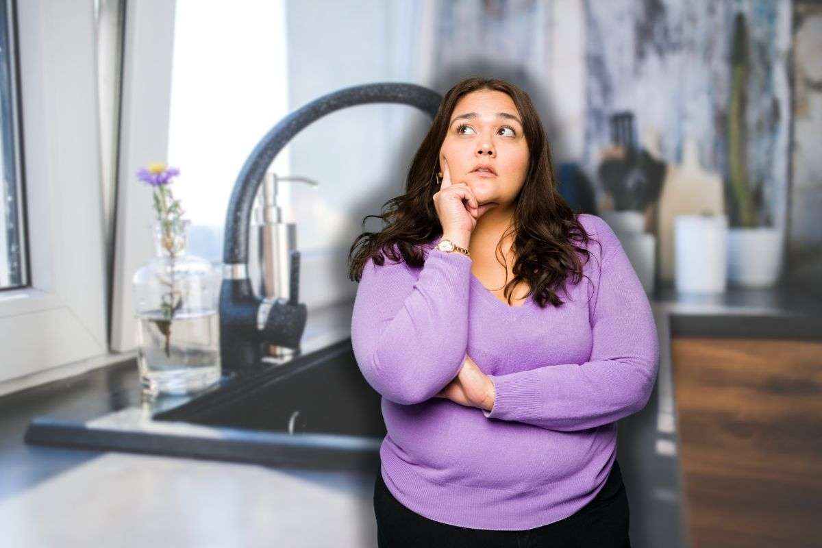 bicchiere di acqua accanto a lavandino e donna che pensa