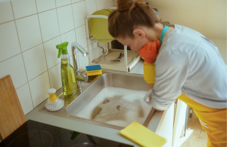donna disperata di fronte a lavandino con scarico ostruito