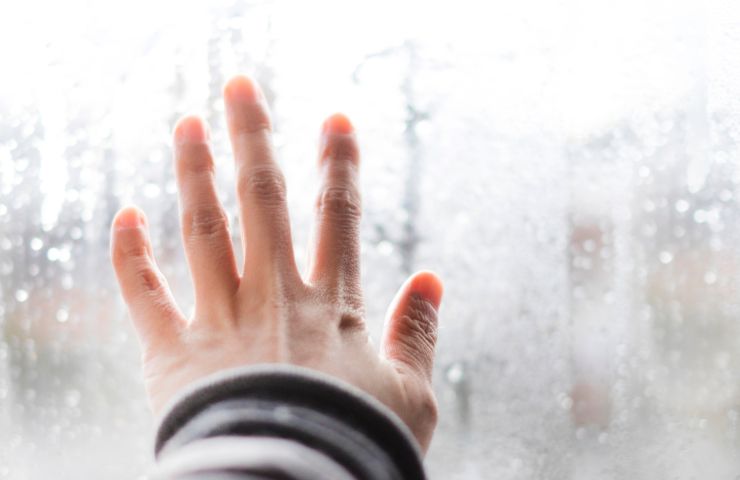 mano che tocca finestra con condensa sui vetri